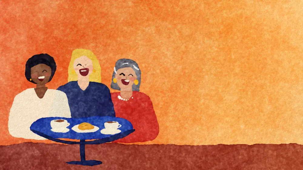 Three women laughing together around a café table.